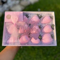 a person holding up a box of pink chocolates with bows on the front and side