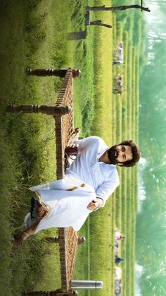 a man standing next to a wooden fence on top of a grass covered field with people in the background