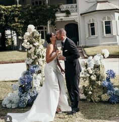 a bride and groom kissing in front of a white house with blue flowers on it