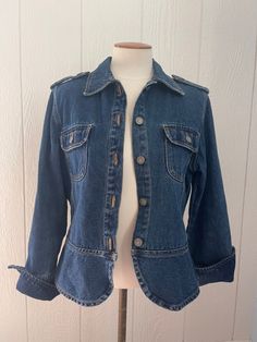 90s military style blue denim jacket. Slightly cropped and fitted. Women’s but could be unisex. Shoulder straps and front pocket detail. Rounded seams on the bottom and fold over cuffs on sleeves. 5 metal buttons down the front as well as on both shoulder straps and front pockets. Condition: Great Size: PS (small) women’s or unisex Brand: BillBlass 100% Cotton Measurements: Total length: 23 1/2” Bust: 42” Fitted Vintage Button-up Denim Top, Fitted Denim Jacket With Flap Pockets, Fitted Utility Denim Jacket With Pockets, Fitted Utility Jacket, Fitted Utility Outerwear In Medium Wash, Fitted Long Sleeve Utility Denim Jacket, Fitted Utility Denim Jacket In Medium Wash, Fitted Utility Denim Jacket, Fitted Blue Denim Jacket With Flap Pockets