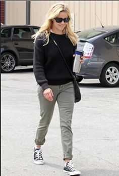 a blonde woman in black sweater and khaki pants holding a coffee cup while walking down the street