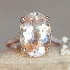 an oval shaped white topazte ring sitting on a rock with flowers in the background