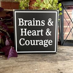 a black and white sign sitting on top of a wooden table next to a potted plant