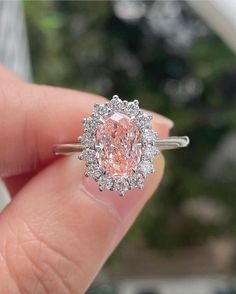 a close up of a person's hand holding a ring with a pink diamond