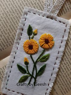 two yellow flowers on a white piece of cloth with green stems and leaves in the center