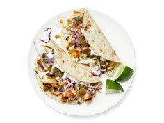 two tacos on a white plate topped with cole slaw and lime wedges