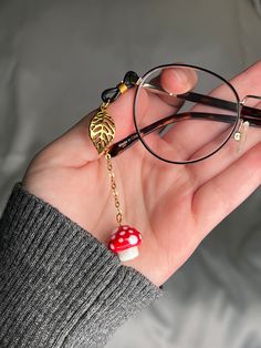 Beautiful mushroom glasses charm: red and white glass mushroom bead on gold-tone chain, with matching metal gold leaf charm.  Single piece made to add to one arm of your glasses.  Silicone loop allows it to easily be added and removed from your glasses to instantly upgrade any outfit! Also available as a full chain: https://www.etsy.com/listing/1370319289/ Approximate chain length: 2 inches. Eye Glasses Accessories, Cute Glasses Accessories, Glasses Accessories Jewelry, Beads Glasses, Mushroom Accessories Aesthetic, Fairy Glasses, Chain For Glasses, Diy Chain Accessories, Glasses Jewelry