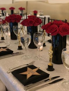 the table is set with red roses in black vases, silverware and napkins