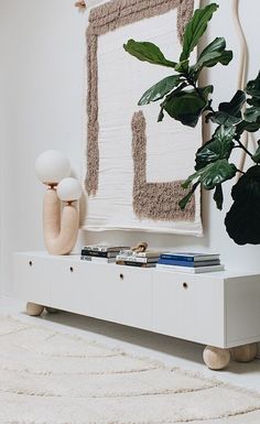 a living room with a plant on top of a white shelf next to a painting