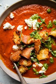 a bowl of tomato soup with bread croutons and garnish on top