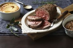 a roast beef sandwich on a plate with two bowls of soup and spoons next to it