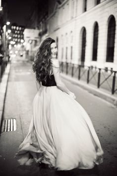 a woman in a long dress walking down the street at night with her back to the camera