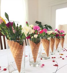 there are five ice cream cones with flowers in them on the table and confetti scattered around