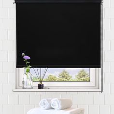 a bathroom with black roller shades on the window and white towels in front of it