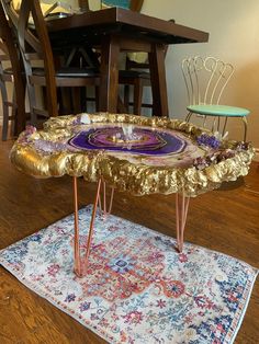 a table made out of gold leaf and purple glass on top of a white rug