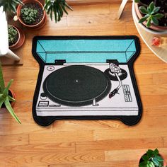 a rug with a turntable on it sitting on a wooden floor next to potted plants