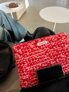 a red purse sitting on top of a couch next to a person's legs