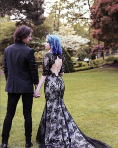 a man and woman in formal wear holding hands while standing next to each other on grass