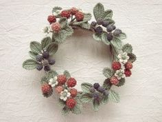 a crocheted wreath with berries and leaves on it sitting on a white surface