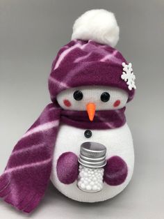 a stuffed snowman with a purple scarf and hat holding a jar in his hands