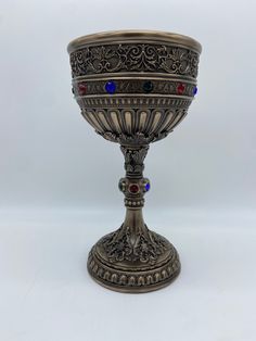 an ornate silver goblet with red, blue and black stones on the rim