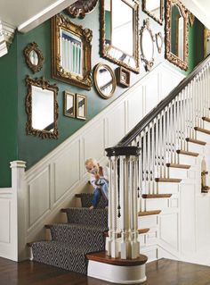 a child sitting on the stairs in front of a staircase with mirrors and framed pictures