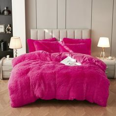 a bed with pink comforter and pillows in a room next to a lamp on the floor