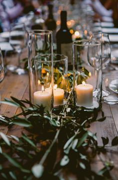 candles are lit on a table with greenery