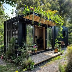 a small black container house in the middle of some trees and grass with plants growing out of it