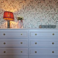 a white dresser sitting next to a lamp on top of a table