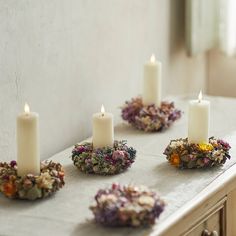 four candles are sitting on a table with dried flowers and wreaths around the candle holders