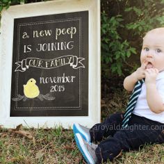 a baby sitting in the grass next to a chalkboard with a sign that says a new peep is coming