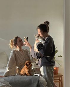 two women sitting on a bed and one is holding a cat while the other holds a dog