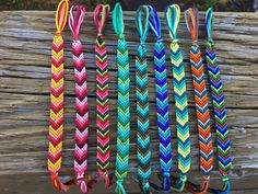 five different colored braided bracelets hanging on a wooden fence