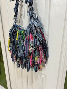 an old pair of jeans hanging from a hook on a white door with multicolored ribbons