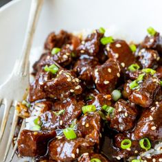 a white plate topped with meat covered in sauce and green onion sprinkles