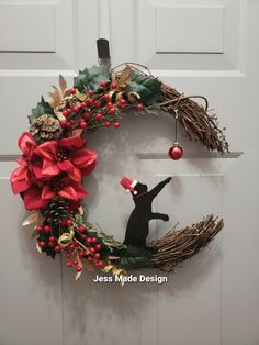 a christmas wreath hanging on the front door with a black cat figurine in it