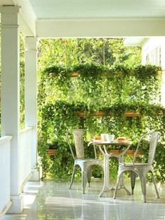 an outdoor dining table and chairs on a porch next to a wall of greenery