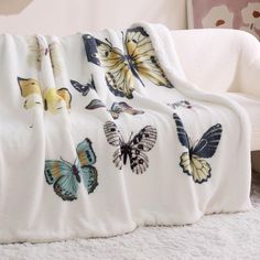 a blanket with butterflies on it sitting on top of a white couch next to a chair