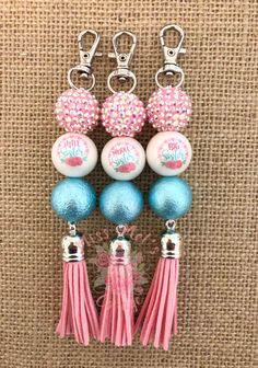 three key chains with different colored balls and tassels hanging from them on a burlap background