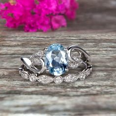 an oval blue topazte and diamond ring on a wooden surface with flowers in the background