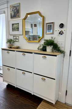 a white dresser topped with lots of drawers next to a wall filled with pictures and plants