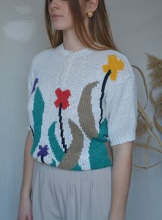 a woman standing in front of a white wall wearing a sweater with flowers on it