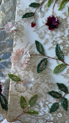 some flowers and green leaves on a white lace tablecloth with red and pink flowers