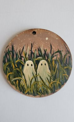 two white birds sitting in tall grass under a brown sky on a wooden wall plaque