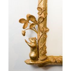 a gold statue of a squirrel on a branch with leaves and flowers in the corner