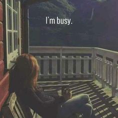 a woman sitting on top of a wooden bench next to a window with the words i'm busy