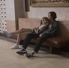 two people sitting on a bench talking on their cell phones in an ornate room with marble walls and flooring