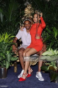 two people sitting on a chair in front of plants and potted plants, posing for the