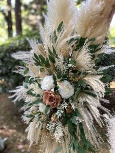 an arrangement of white flowers and greenery in a vase on a tree stump outside